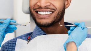 Person with white teeth smiling next to a dentist with gloves holding tools.
