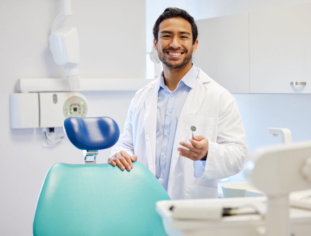 Friendly male dentist next to an exam chair.
