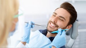 Female dentist holding tools next to a smiling man in a dental exam chair.