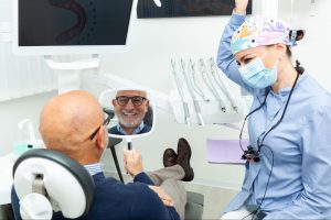 Man looking at his smile in a mirror next to a female dentist.