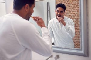 Man brushing his teeth and looking at himself in the mirror.