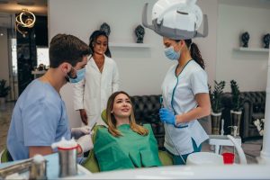 A female patient is being checked by a male cosmetic dentist with the assistance of medical staff.