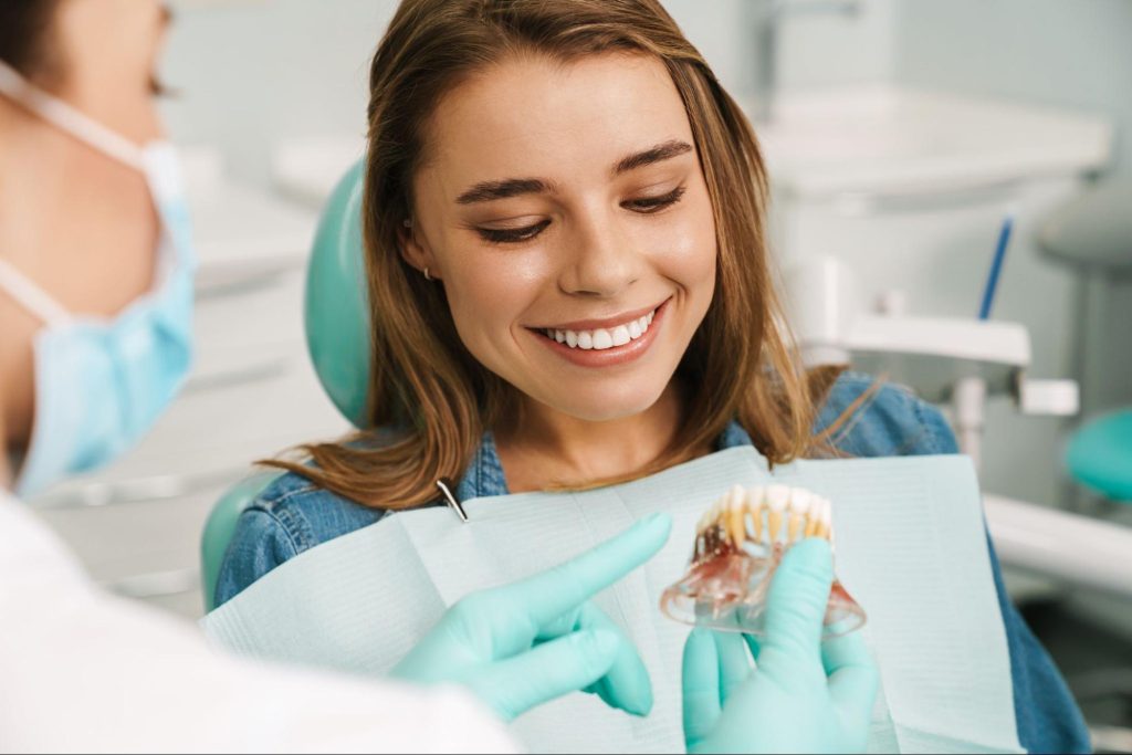 A female dentist uses a dental model to explain the dental implant procedure to her patient, who smiles.