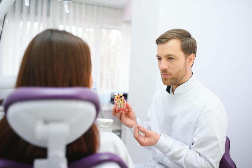 A male dentist uses a dental model to discuss the dental implant process with a patient.
