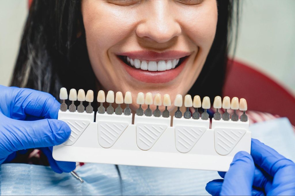 A woman with a bright smile selects her tooth shade for veneers treatment.