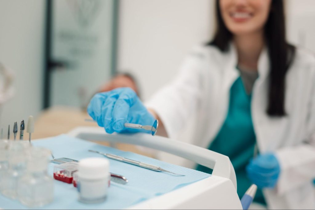 A female dentist reaching for a dental mirror to begin an oral checkup.