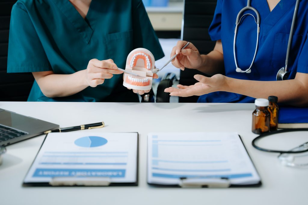 Two dentists demonstrate proper tooth brushing as part of a health plan.