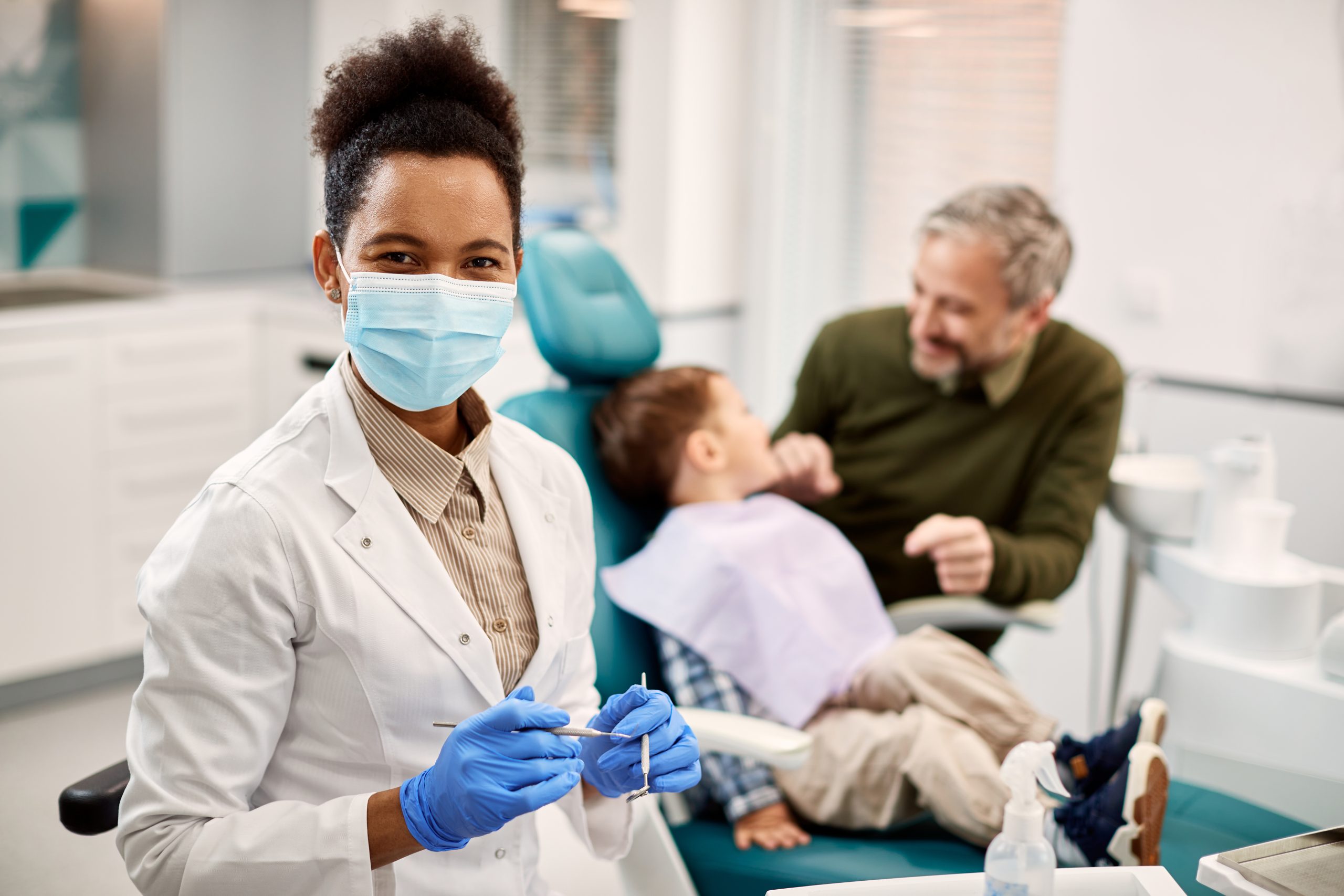A family dentist poses in front of two of her patients, a father and son.