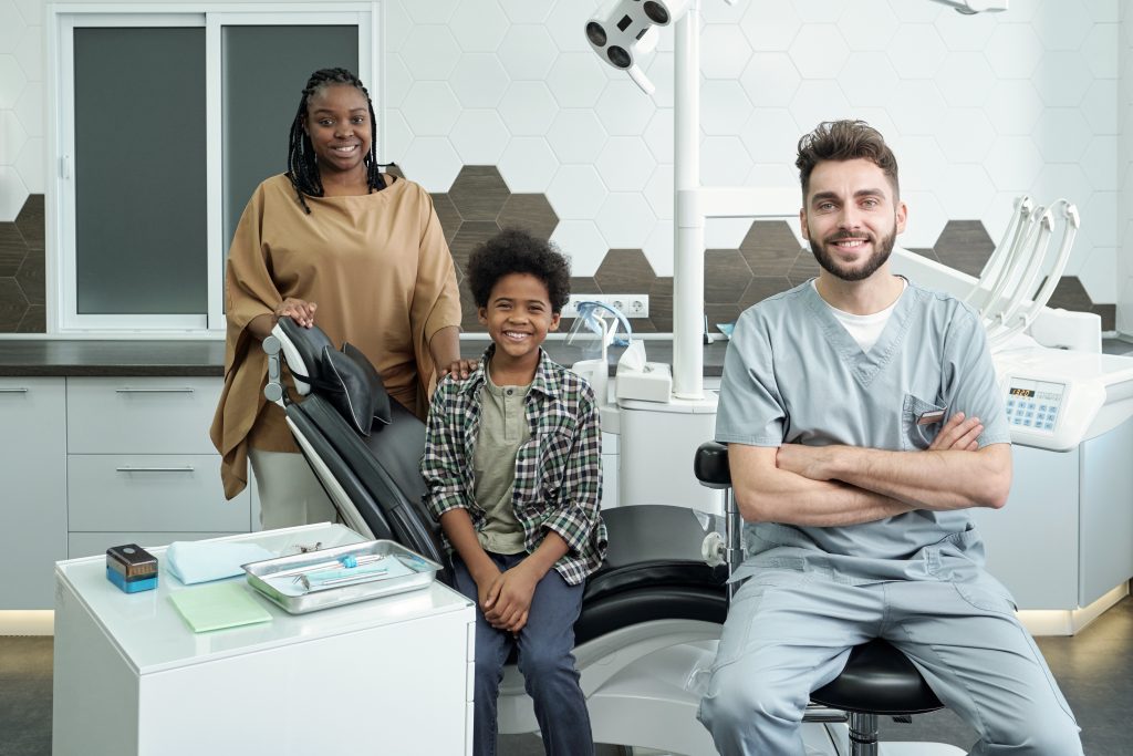 A dentist poses with two of his patients, a mother and her son.