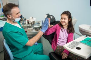 A child and her pediatric dentist high-five before an exam.