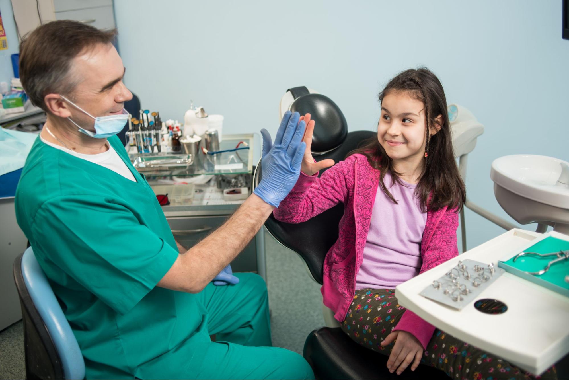 A child and her pediatric dentist high-five before an exam.