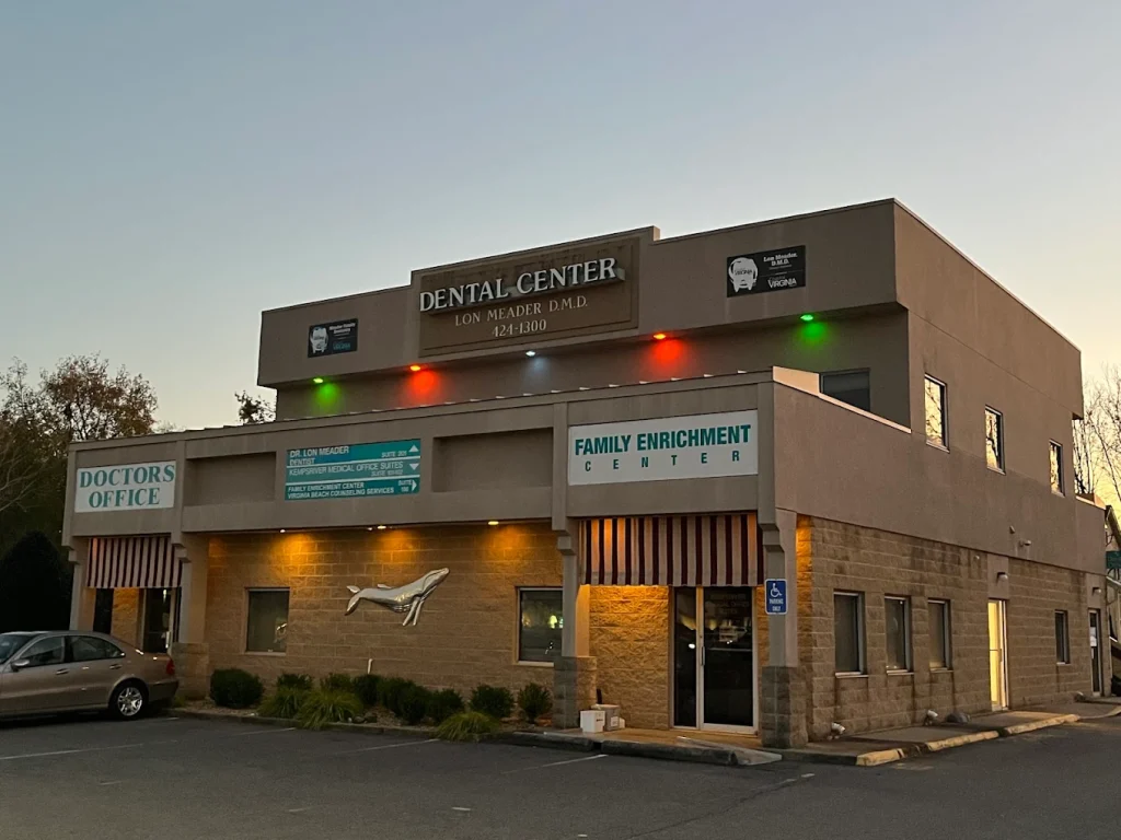 Exterior view of a two-story dental clinic with signs reading 'Dental Center' and 'Doctors Office' during dusk, showing parked car and entryway.